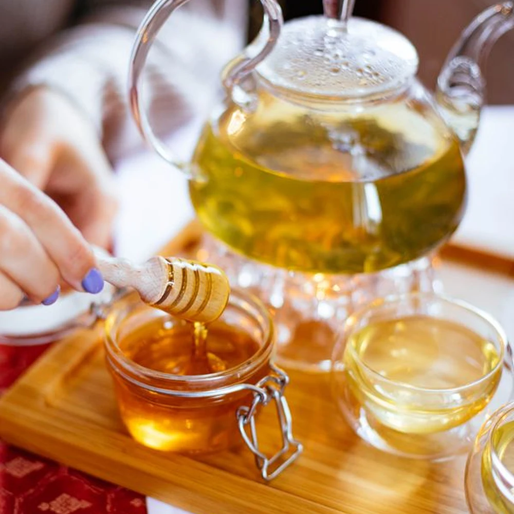 Honey jar and dipper beside a glass teapot